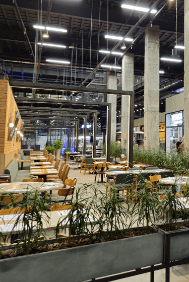 Vista da praça de alimentação da Denim City SP com suas mesas e cadeiras além de várias plantas ao redor